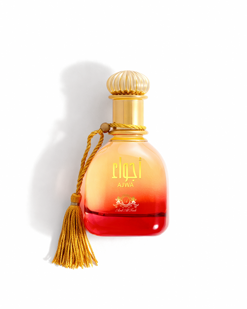 Ajwa perfume by Ard Al Teeb in a red-to-golden gradient glass bottle with a gold tassel and decorative gold cap on a white background.